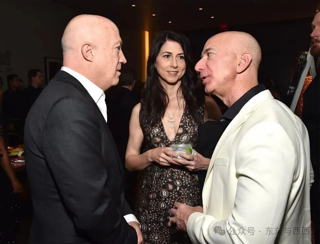 Jeff Bezos in white suit and then-MacKenzie Bezos in patterned dress speaking with Brian Lourd in black suit at a benefit gala in 2018.