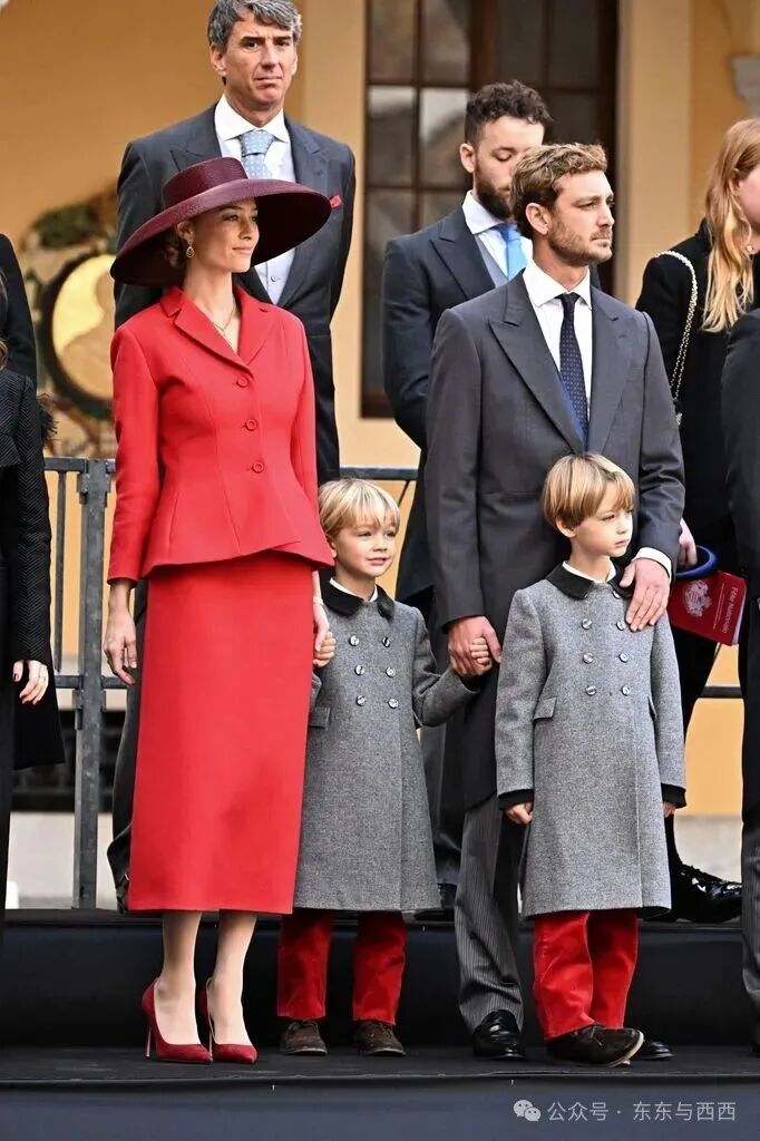 Beatrice Borromeo stands with her family in a red structured suit and matching wide-brim hat, coordinating with her sons' red velvet trousers.