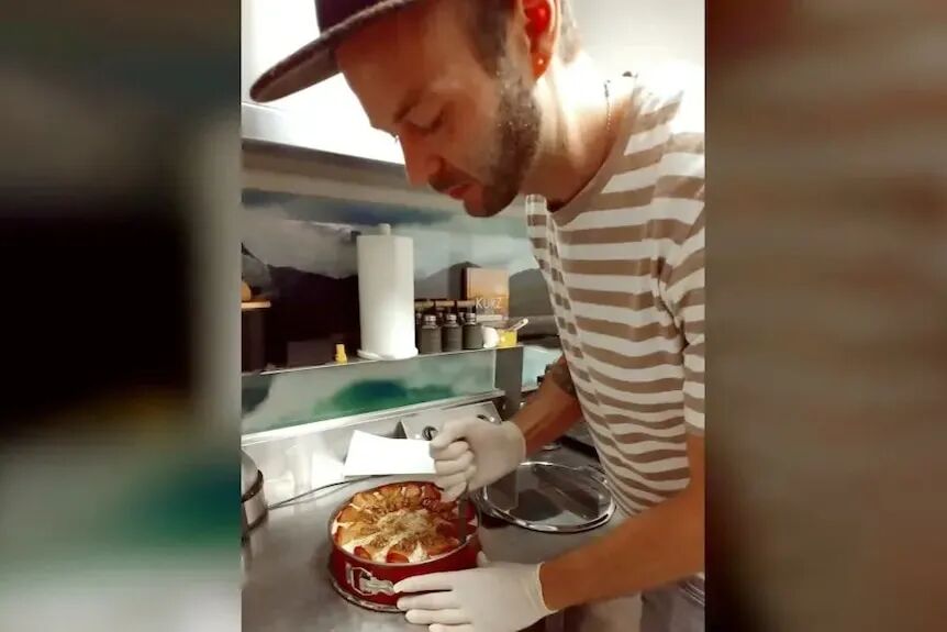 一位留着短胡子的年轻男子在商业厨房里切蛋糕。