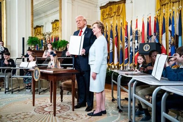 在签署行政命令的仪式上，特朗普总统坐在教育部长琳达·麦克马洪旁边。几名学童坐在他们身后。